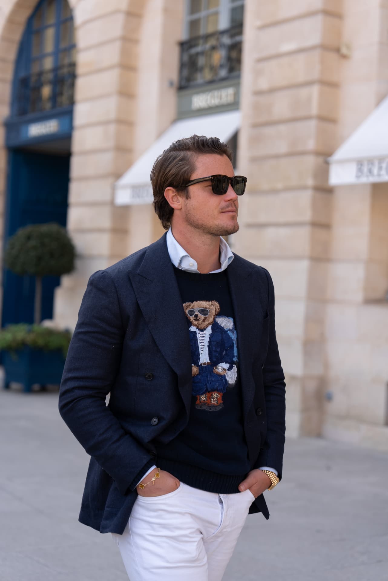 Robert Nass in een donkerblauwe blazer en zonnebril op straat, met zandstenen gebouwen en winkelpuien op de achtergrond